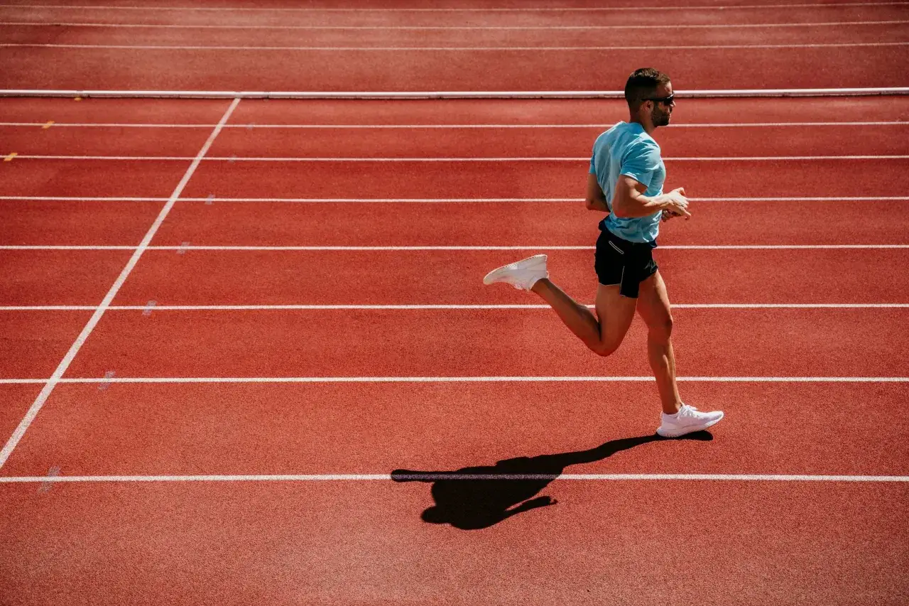 Atleta corre in pista, puntando a un ritmo di 4 minuti al km. La sua ombra si allunga sulla corsia rossa.