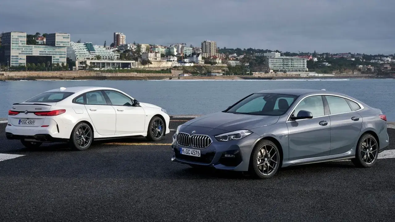 Dwa BMW 235i, białe i szare, stoją na tle nadmorskiego miasta.