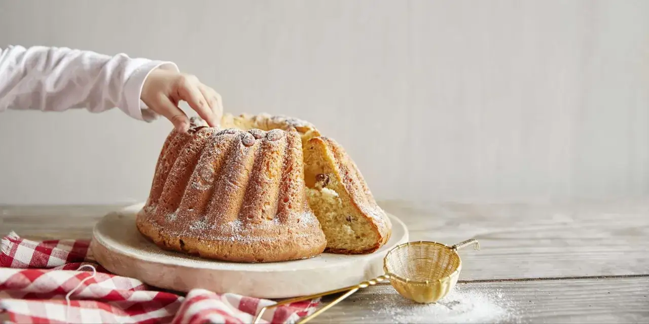 Une main d'enfant effleure un savoureux gâteau en forme de couronne, une délicieuse entrée alsacienne saupoudrée de sucre glace.