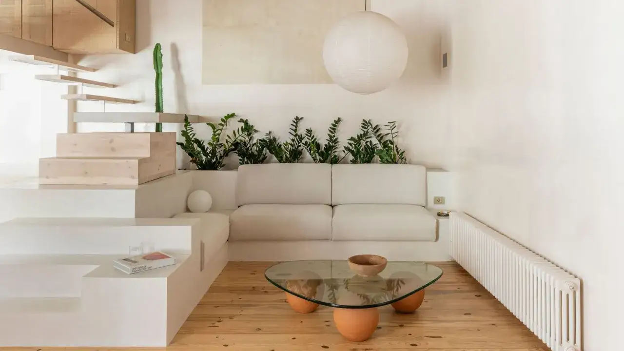 Salon au style wabi sabi, avec un canap&eacute; blanc, des plantes vertes, une table basse en verre et bois, et un escalier en bois brut.