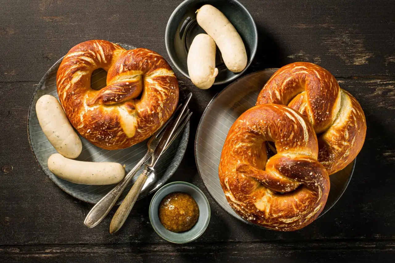 Zwei Teller mit knusprigen Sauerteig Brezeln, dazu Weißwürste und Senf. Ein herzhafter Genuss!