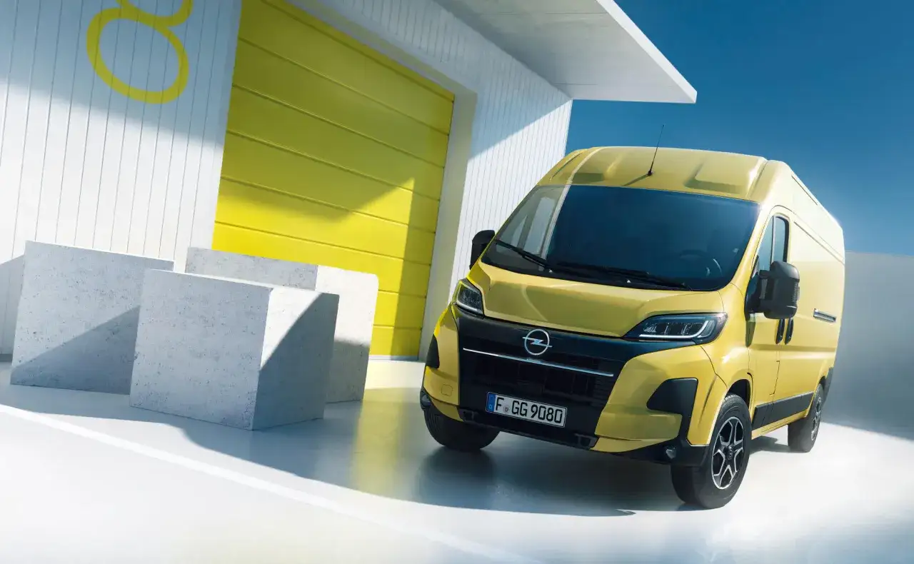 En gul Opel skåpbil, en av många Opel modeller, står parkerad framför en gul port och vita byggnader.