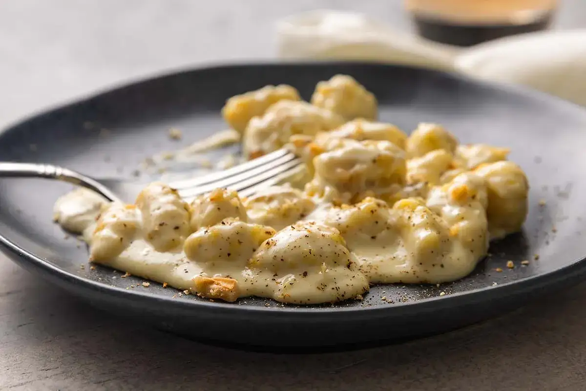 Gnocchi in cremiger Gorgonzola-Sauce, bestreut mit Pfeffer und Nüssen, auf einem dunklen Teller mit einer Gabel.