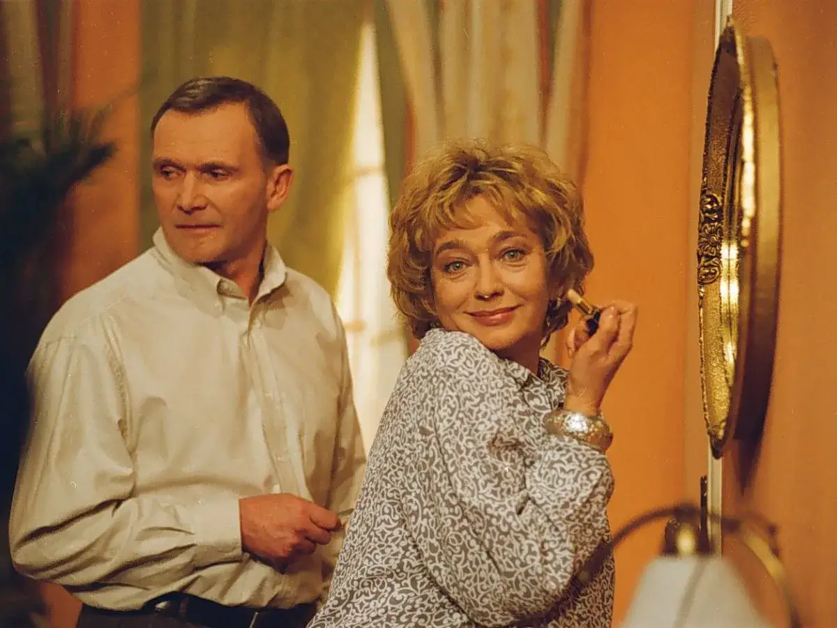 Ewa Szykulska w jednym z filmów, maluje usta przed złotym lustrem, obok stoi mężczyzna.