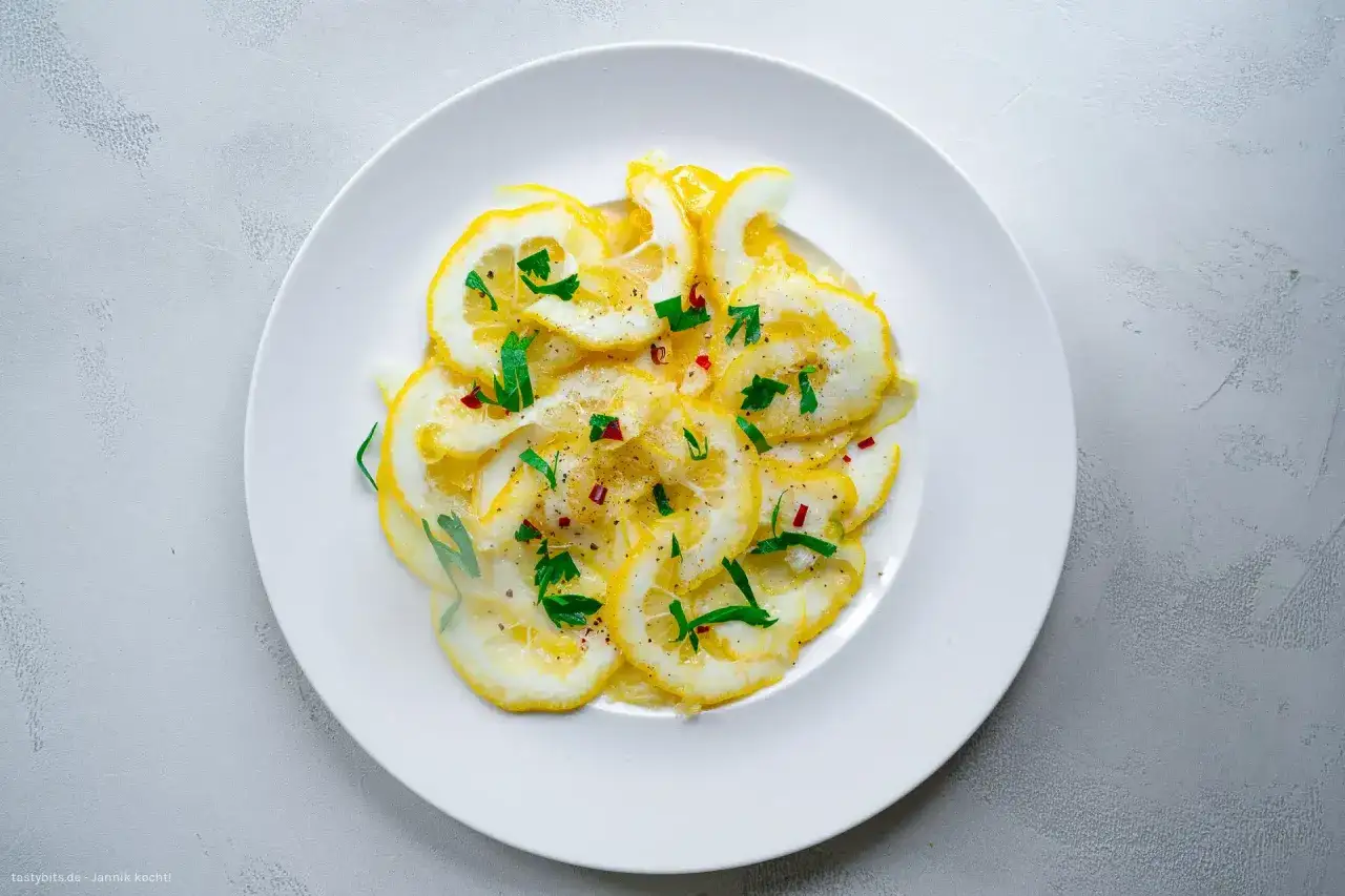 D&uuml;nne Scheiben Zitrone mit Zucker bestreut, garniert mit frischen Kr&auml;utern und roten Chiliflocken. Ein erfrischender Genuss!