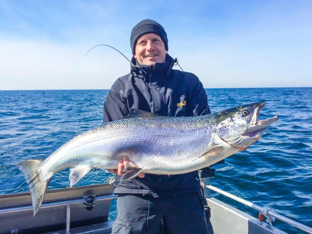 Gl&uuml;cklicher Angler h&auml;lt riesigen Lachs auf dem Meer. Ein toller Fang, der zeigt, wo man Lachs angeln kann!