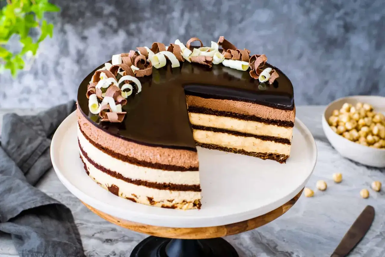 Una golosa torta Savoia a più strati, con mousse al cioccolato e crema, decorata con riccioli di cioccolato bianco e fondente.