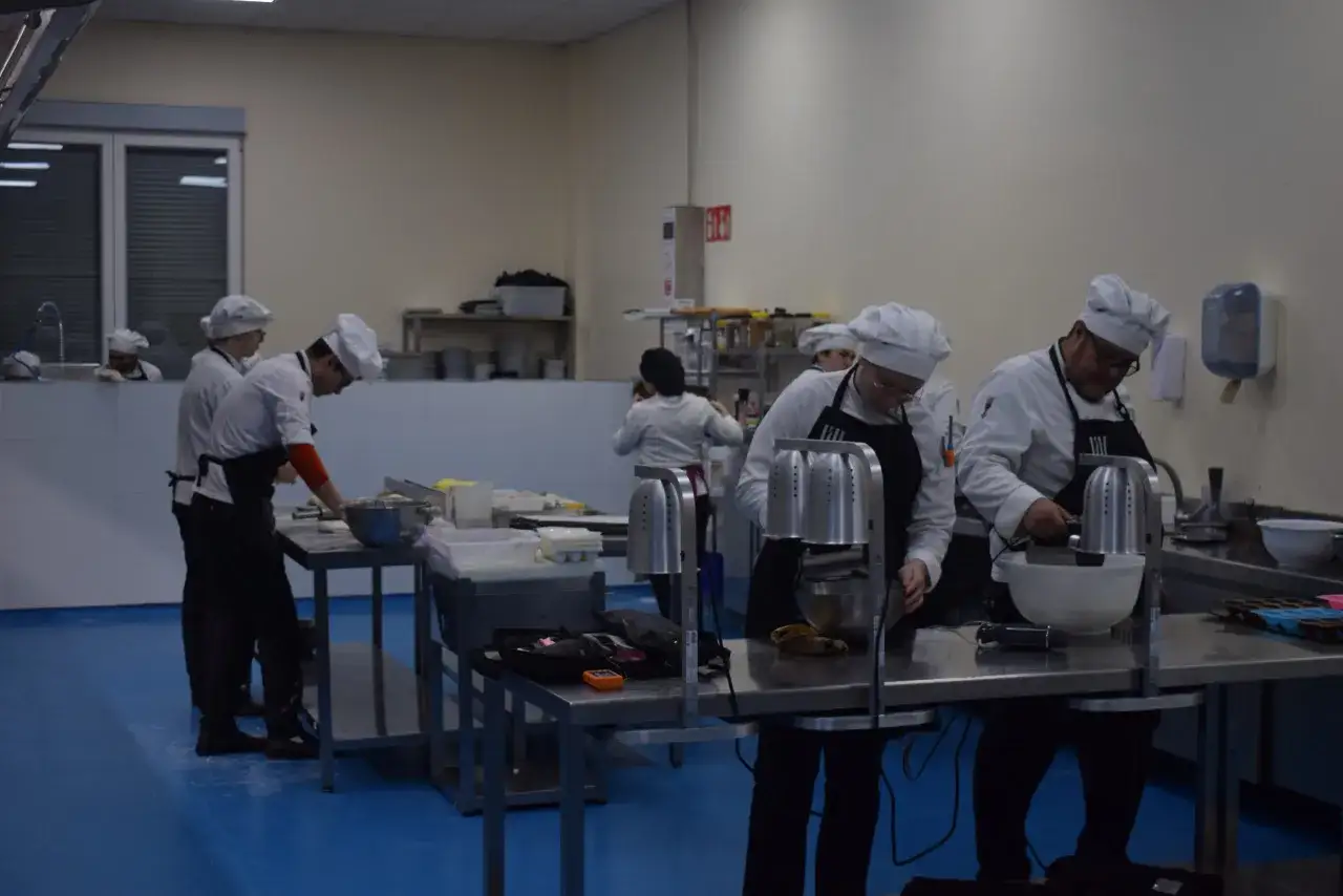 Estudiantes de ciencias culinarias y gastron&oacute;micas practican en una cocina profesional, preparando ingredientes y usando batidoras.