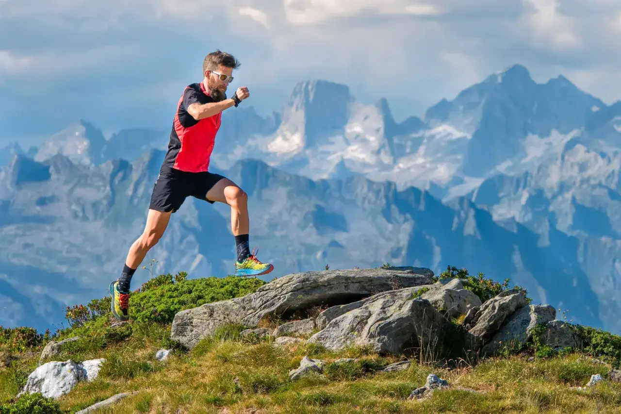 Corredor de trail running en la monta&ntilde;a, con un paisaje alpino de fondo. Sus movimientos sugieren ejercicios de fuerza para trail running.