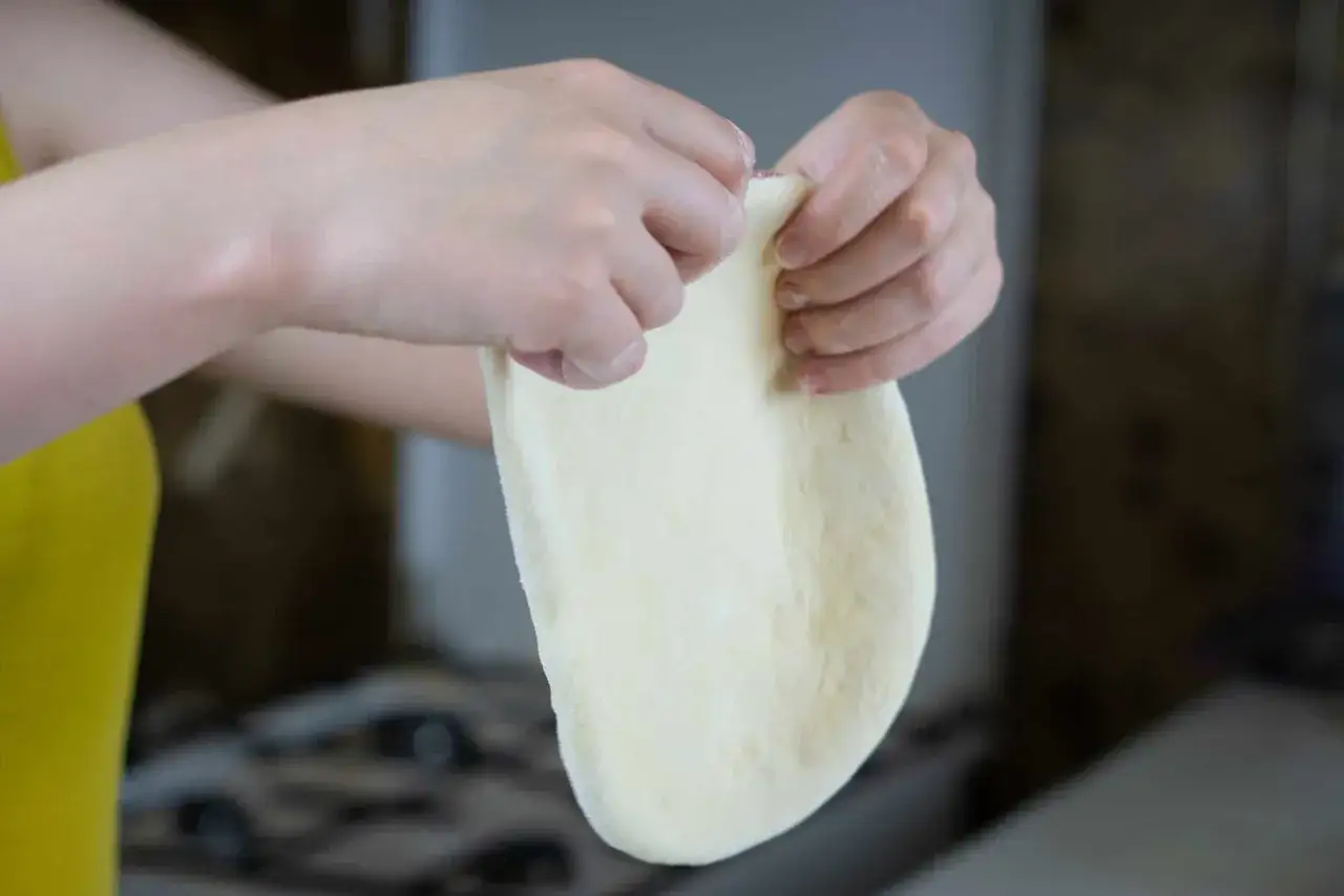 Dłonie formują elastyczne ciasto na pizzę, przygotowując je do pieczenia.