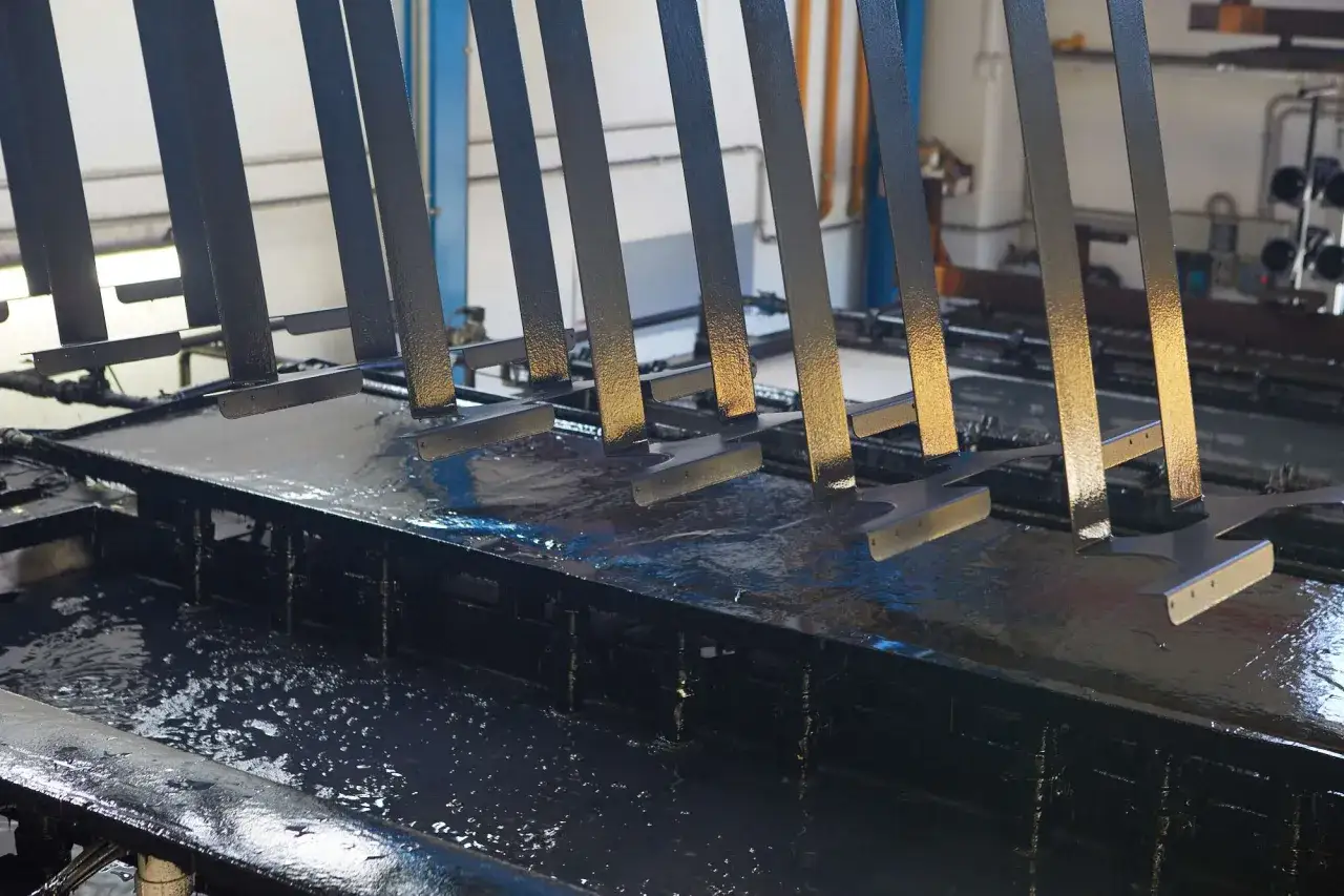 Parti metalliche immerse in un bagno scuro, probabilmente per un trattamento fosfatante.
