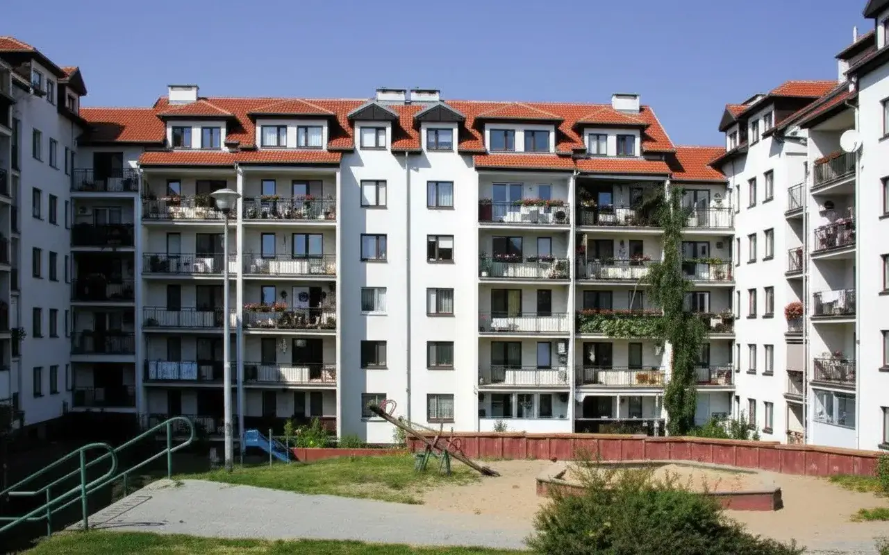 Nowoczesne bloki mieszkalne w Gdańsku. Na pierwszym planie plac zabaw z piaskownicą i huśtawką.