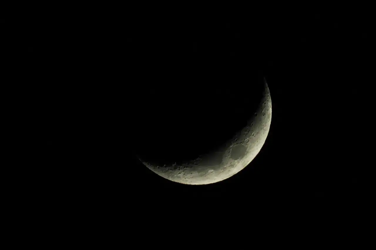 Srebrny sierp księżyca na czarnym niebie, przypominający o tym, kiedy jest Ramadan.