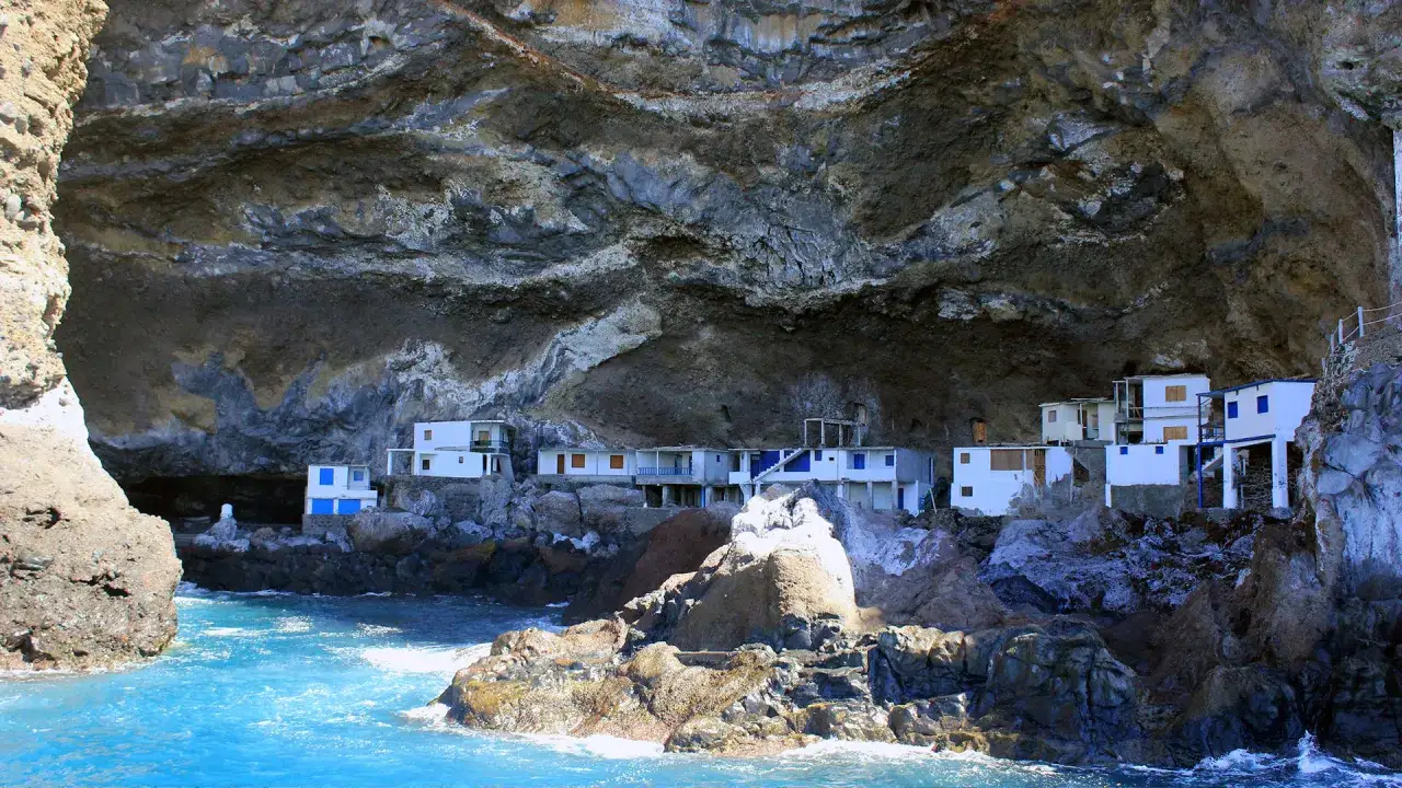 Casitas blancas con techos azules se aferran a la roca bajo un gran acantilado en los poris de Candelaria, La Palma.