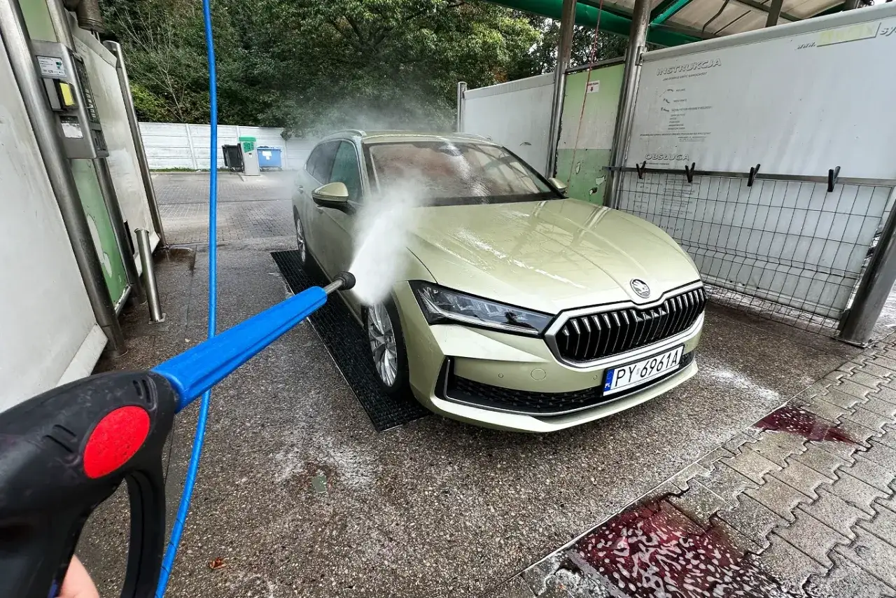 Mycie auta na samoobsługowej myjni. Woda pod ciśnieniem spływa po masce, pokazując, czym umyć auto domowe sposoby.