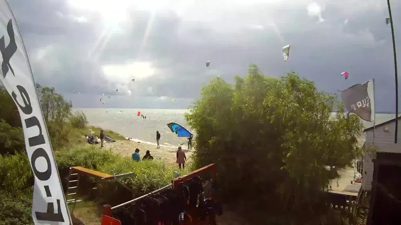 Ekolaguna Chałupy tętni życiem, kitesurferzy szybują nad wodą, a plażowicze cieszą się słońcem.