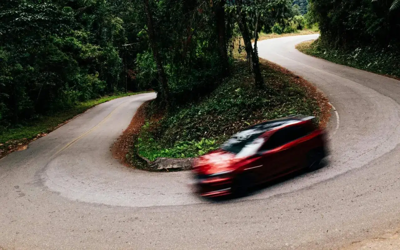 Auto rossa in curva su strada tortuosa tra alberi. Il **freno motore** aiuta a controllare la velocit&agrave; in discesa.