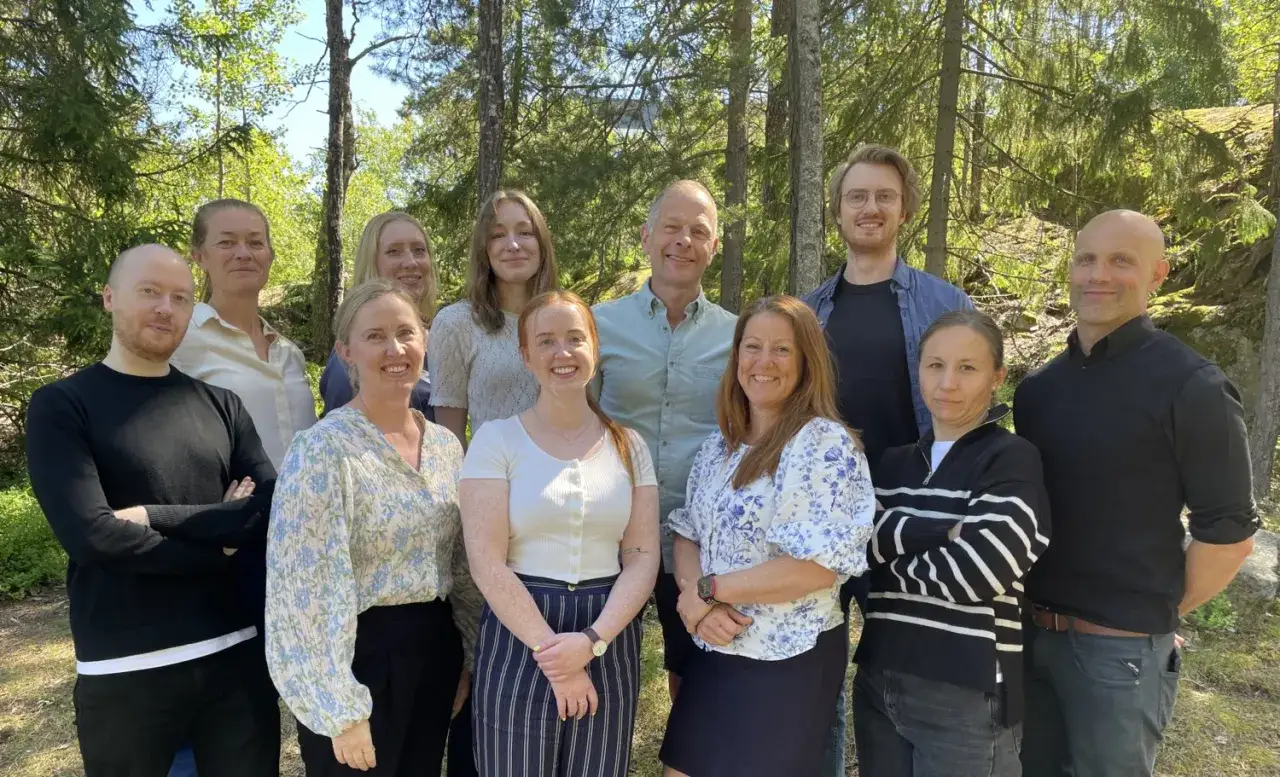 En grupp glada kollegor, inklusive Tobias Sahlin, poserar utomhus i skogen.