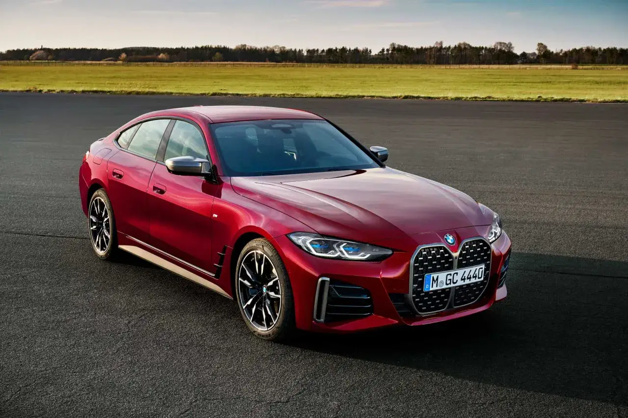 Czerwone BMW 4 Gran Coupé na tle zielonych pól i błękitnego nieba. Elegancka linia nadwozia i sportowe detale.