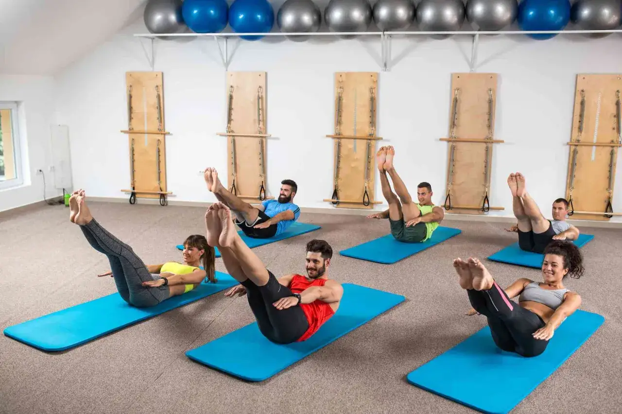 Gente practicando yogalates que es una disciplina que combina yoga y pilates, en un estudio con equipos de pilates y balones de ejercicio.