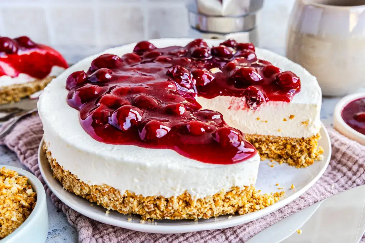 Cremiger 10 min kuchen ohne backen mit Kirschtopping. Ein Stück ist bereits angeschnitten.