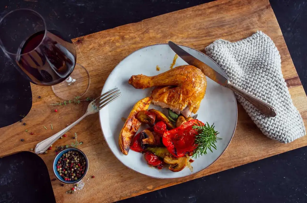 Un verre de vin rouge accompagne un poulet r&ocirc;ti savoureux avec des l&eacute;gumes grill&eacute;s. Quel vin avec poulet r&ocirc;ti ? Un Pinot Noir serait parfait.