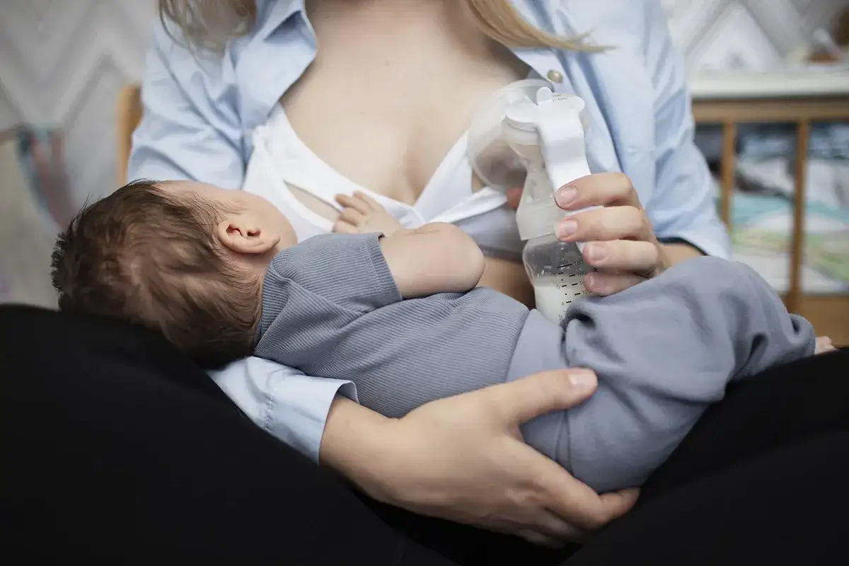 Mama karmi dziecko piersią i butelką, stosując karmienie mieszane. Dziecko śpi wtulone w ramiona mamy.
