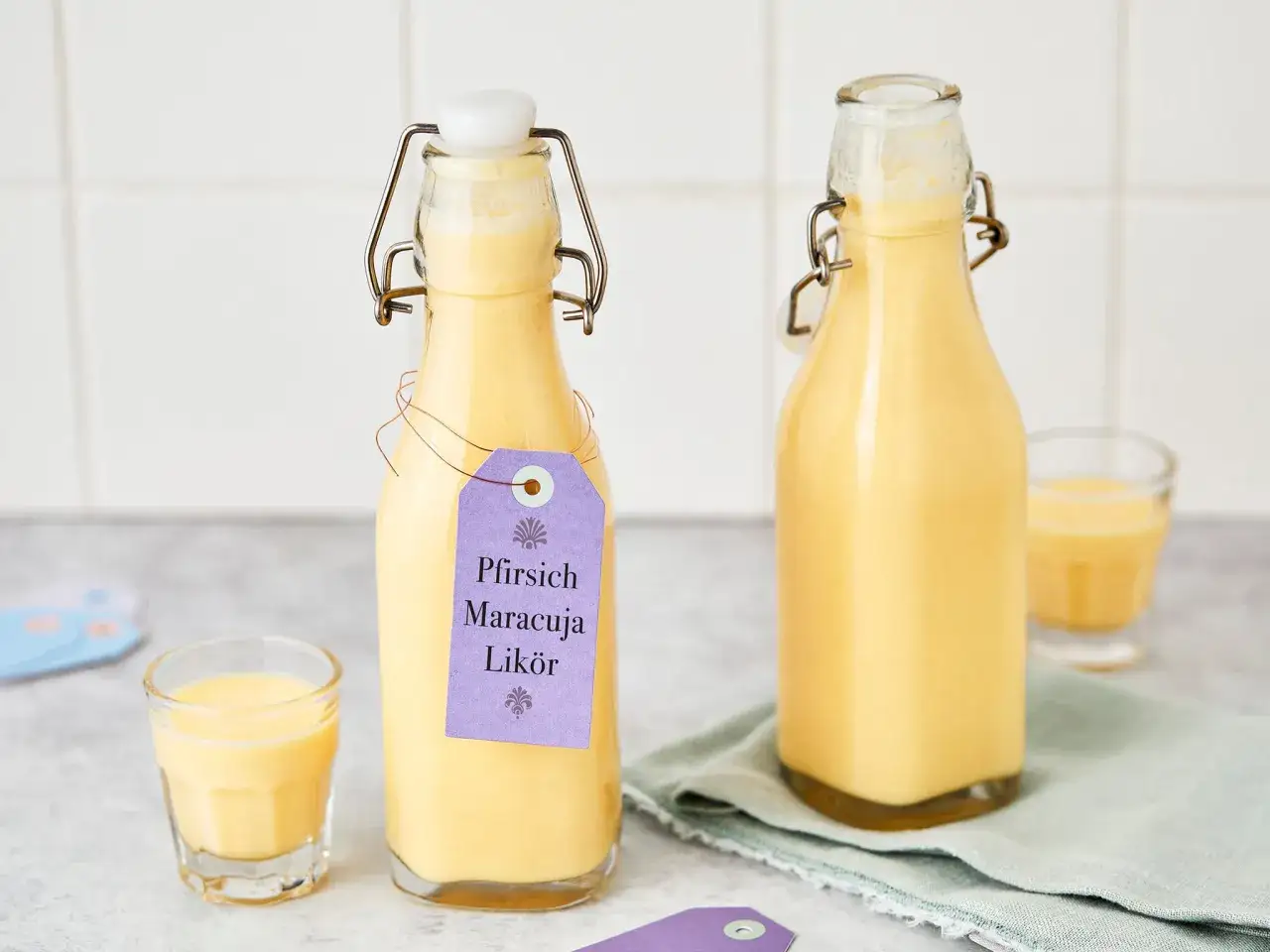 Zwei Flaschen Pfirsich-Maracuja-Lik&ouml;r, ein cremiges Solero Schnaps Rezept ohne Sahne. Ein kleines Glas ist gef&uuml;llt.