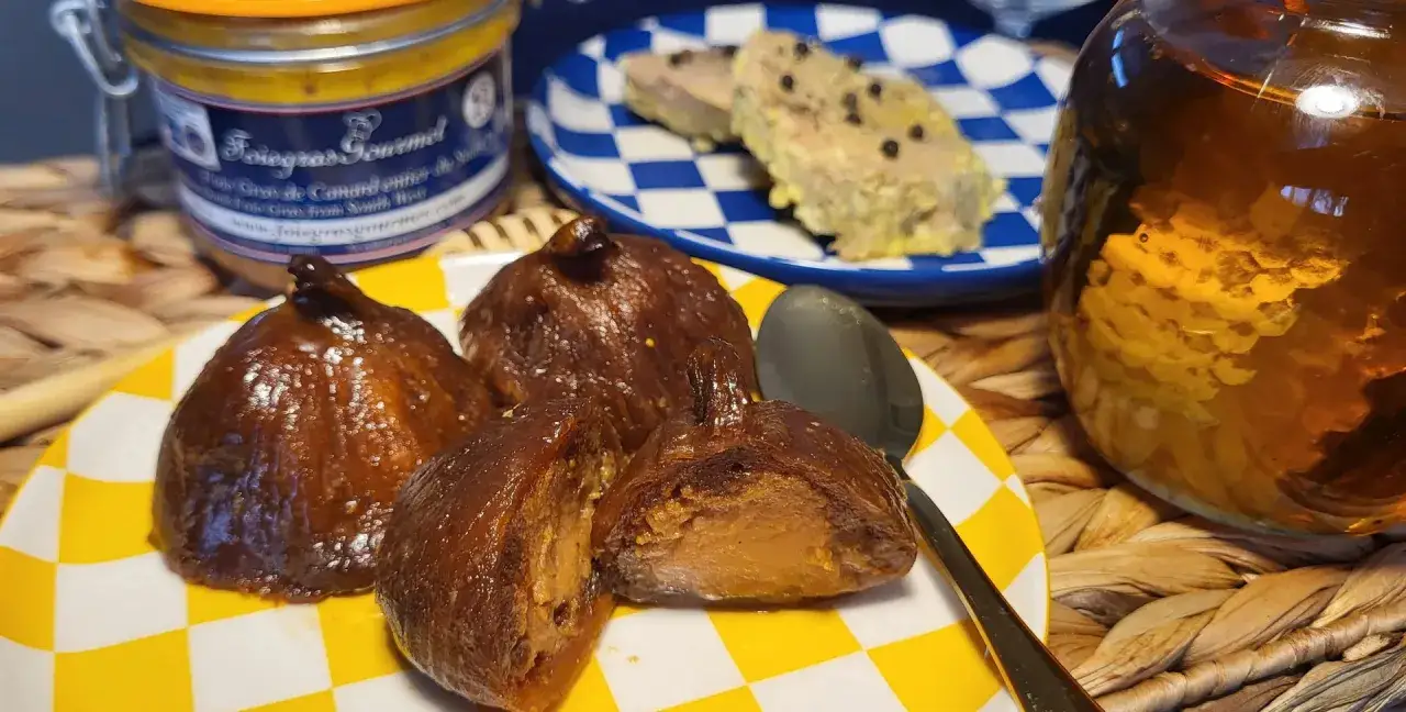 Higos glaseados, uno cortado, junto a un tarro de foie gras y una jarra dorada.