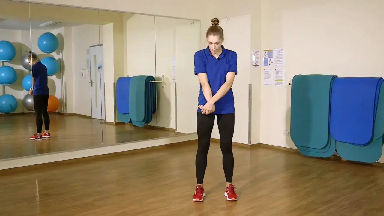 Frau dehnt ihren Arm, um den Tennisarm zu lindern. Sie steht in einem Gymnastikraum mit Spiegeln und Gymnastikb&auml;llen.