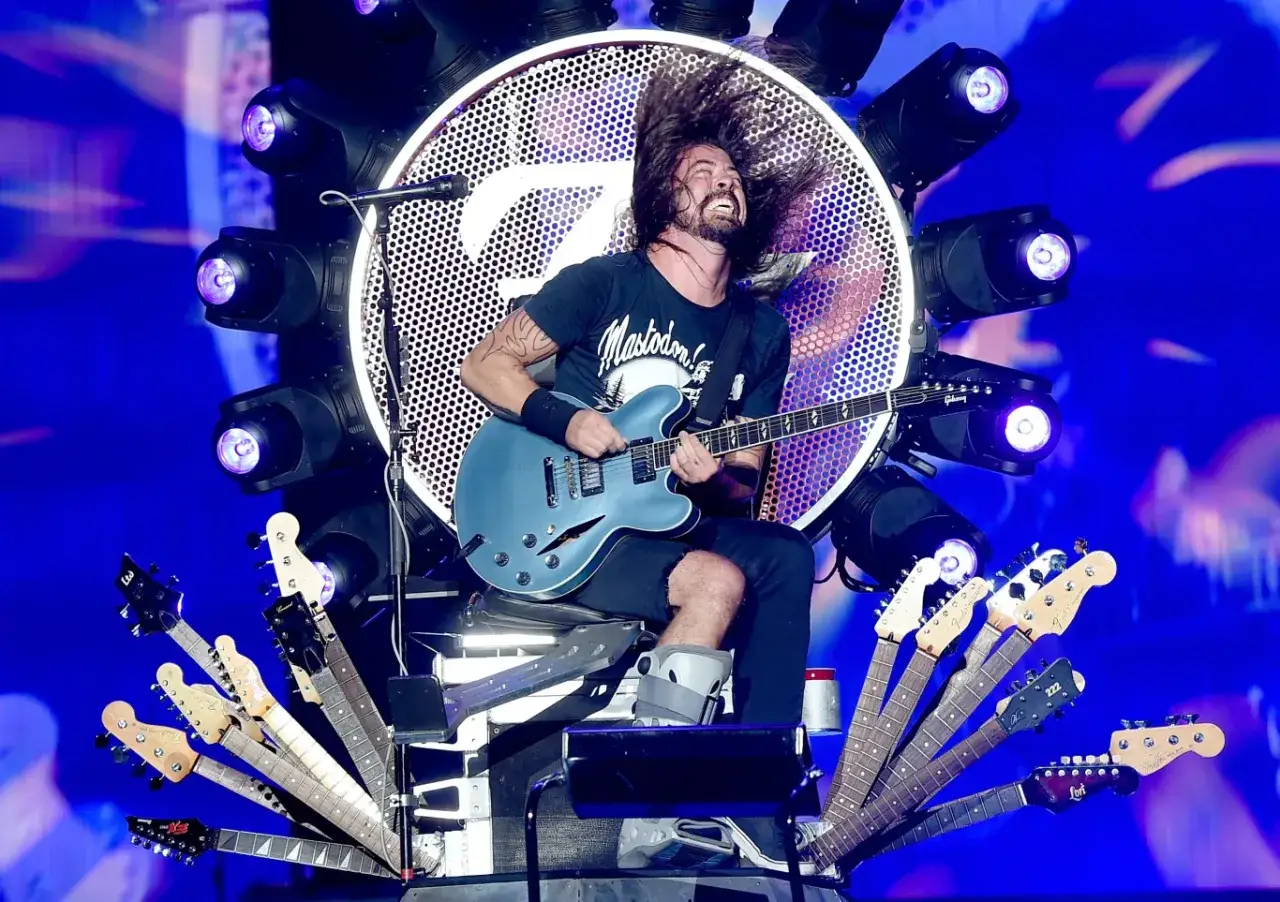 Dave Grohl z zespołem Foo Fighters na scenie, grając na gitarze z włosami w powietrzu.