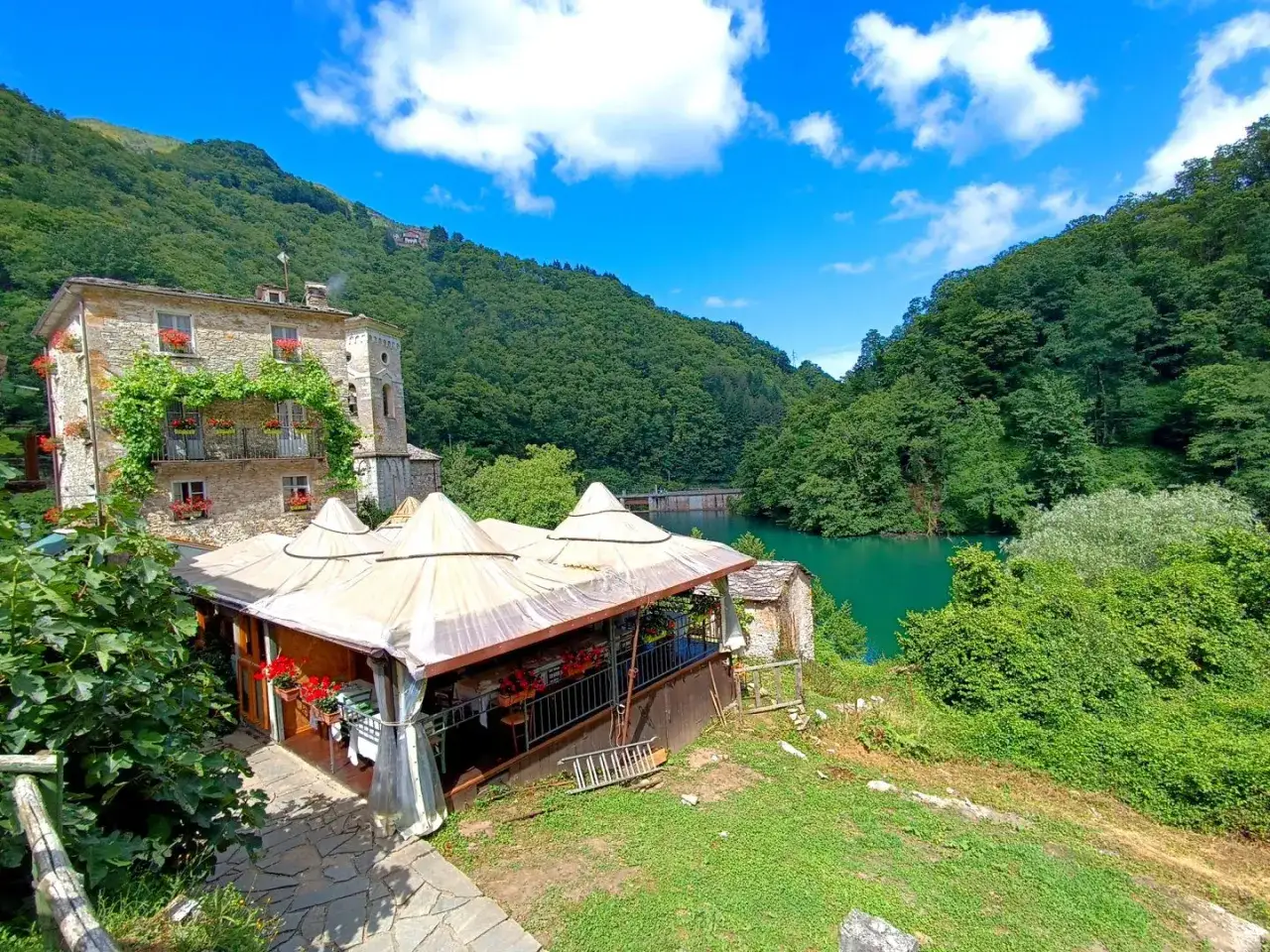 Un antico edificio in pietra con balconi fioriti domina un lago verde smeraldo. Un ristorante all'aperto invita a scoprire **Careggine cosa vedere**.