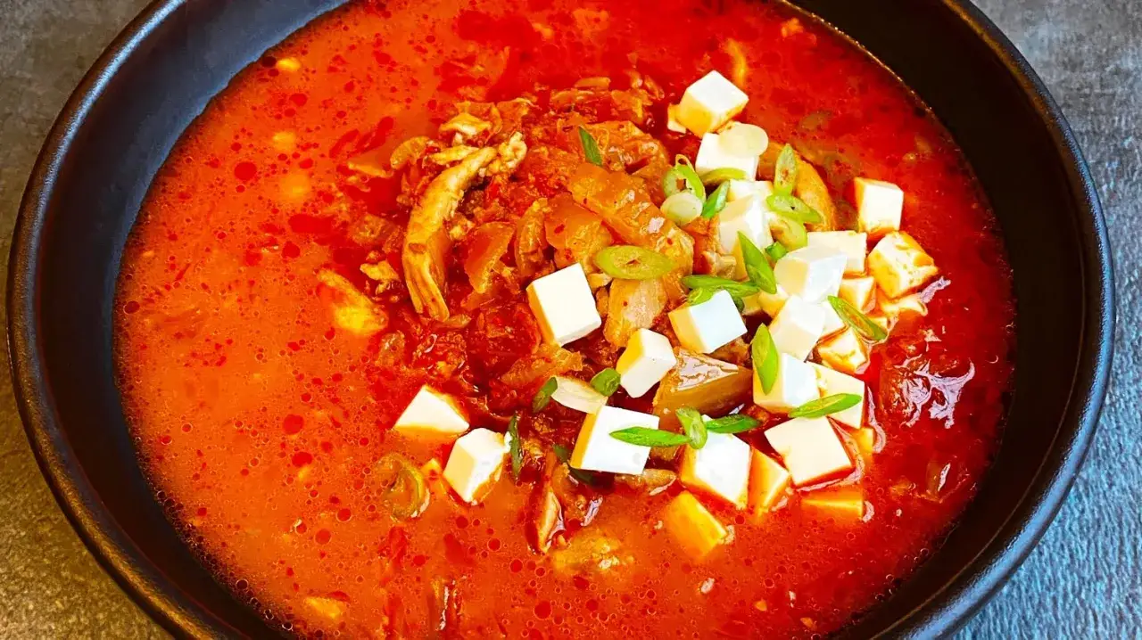 Pikantne, czerwone kimchi jjigae z kostkami tofu i zieloną cebulką. Idealny przepis na rozgrzewający posiłek.