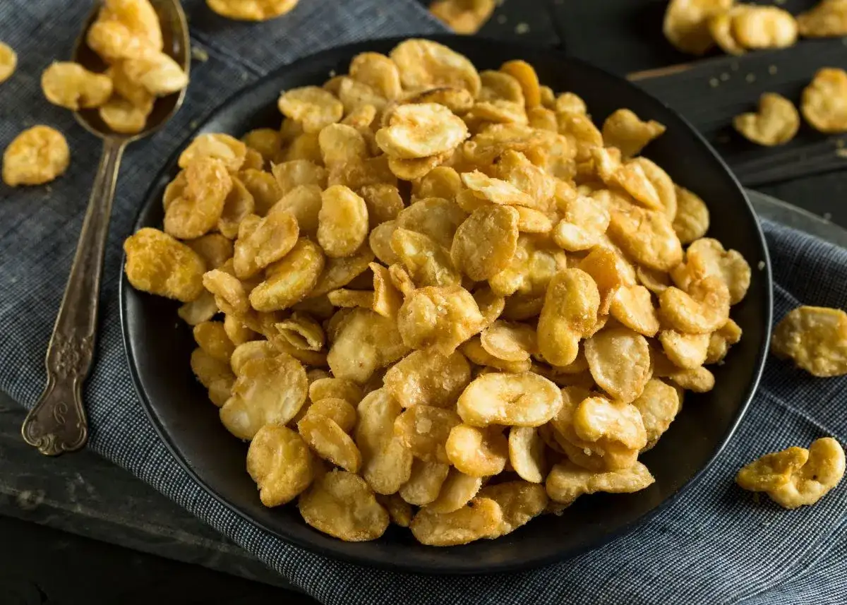Un plato lleno de crujientes habas fritas, doradas y listas para disfrutar. Una cuchara a la izquierda muestra m&aacute;s de este delicioso aperitivo.