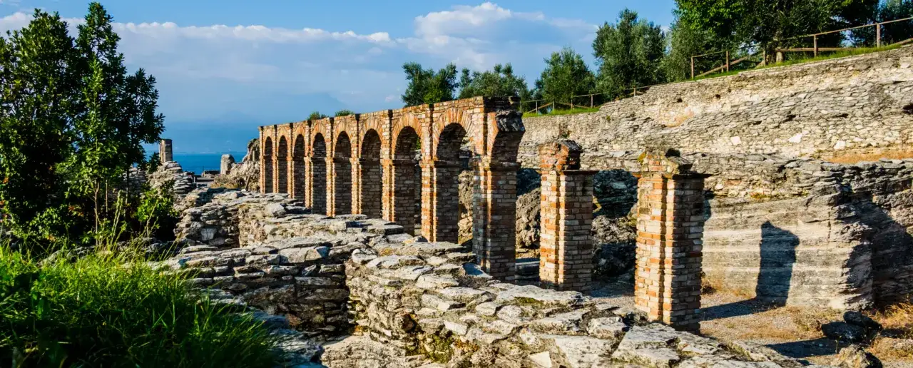 Antiche rovine delle Grotte di Catullo, con archi in mattoni e muretti in pietra che si affacciano sul lago.