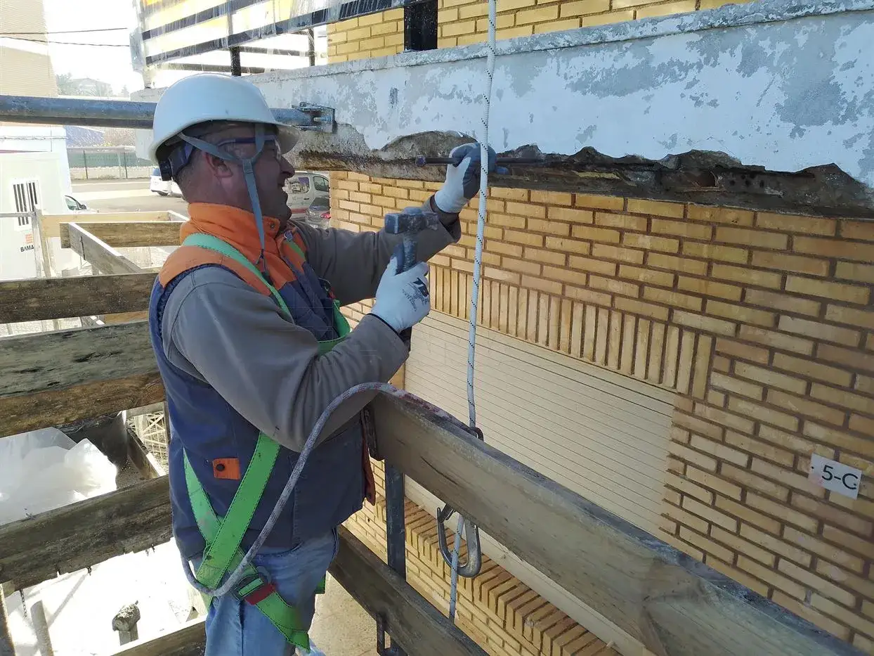 Obrero en andamio repara fachada da&ntilde;ada por humedad por filtraci&oacute;n.