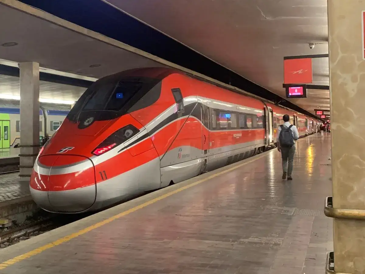 Un train rouge vif prêt à partir de Rome pour Florence. Un voyageur avec un sac à dos attend sur le quai.