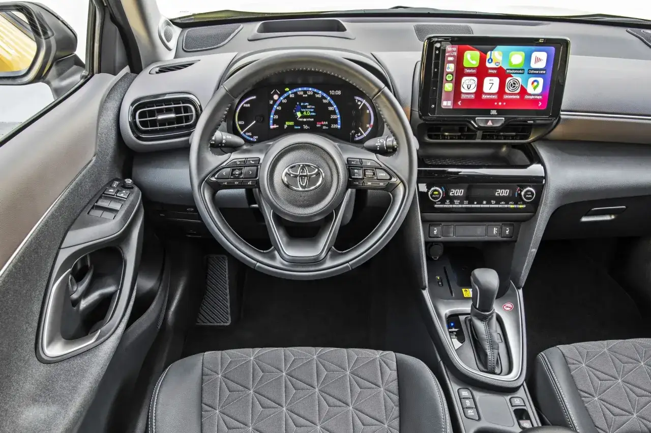 Wnętrze Toyoty Yaris Cross. Kierownica, ekran multimediów z Apple CarPlay, panel klimatyzacji. Opinie o tym modelu są pozytywne.