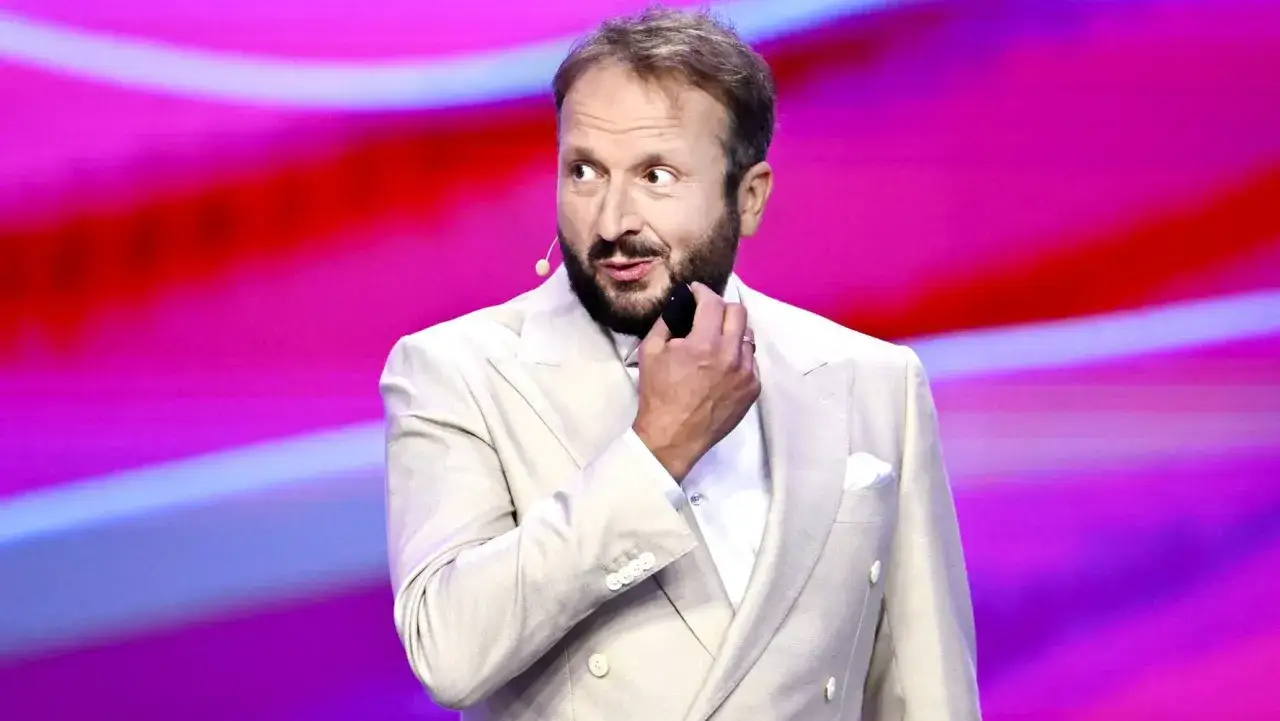 Komik w jasnym garniturze, zastanawiający się, dlaczego przestał pić alkohol i jak to wpłynęło na jego żarty.
