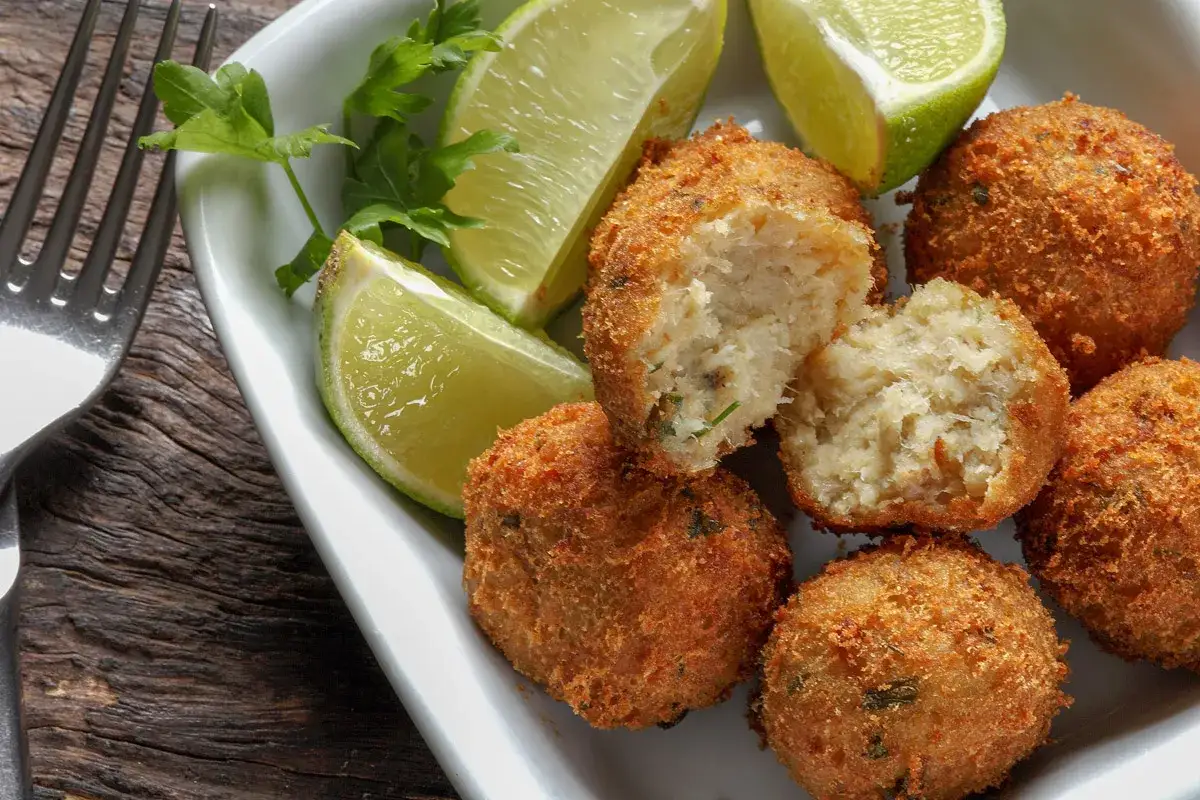 Polpette di merluzzo dorate e croccanti, servite con spicchi di lime e prezzemolo fresco.