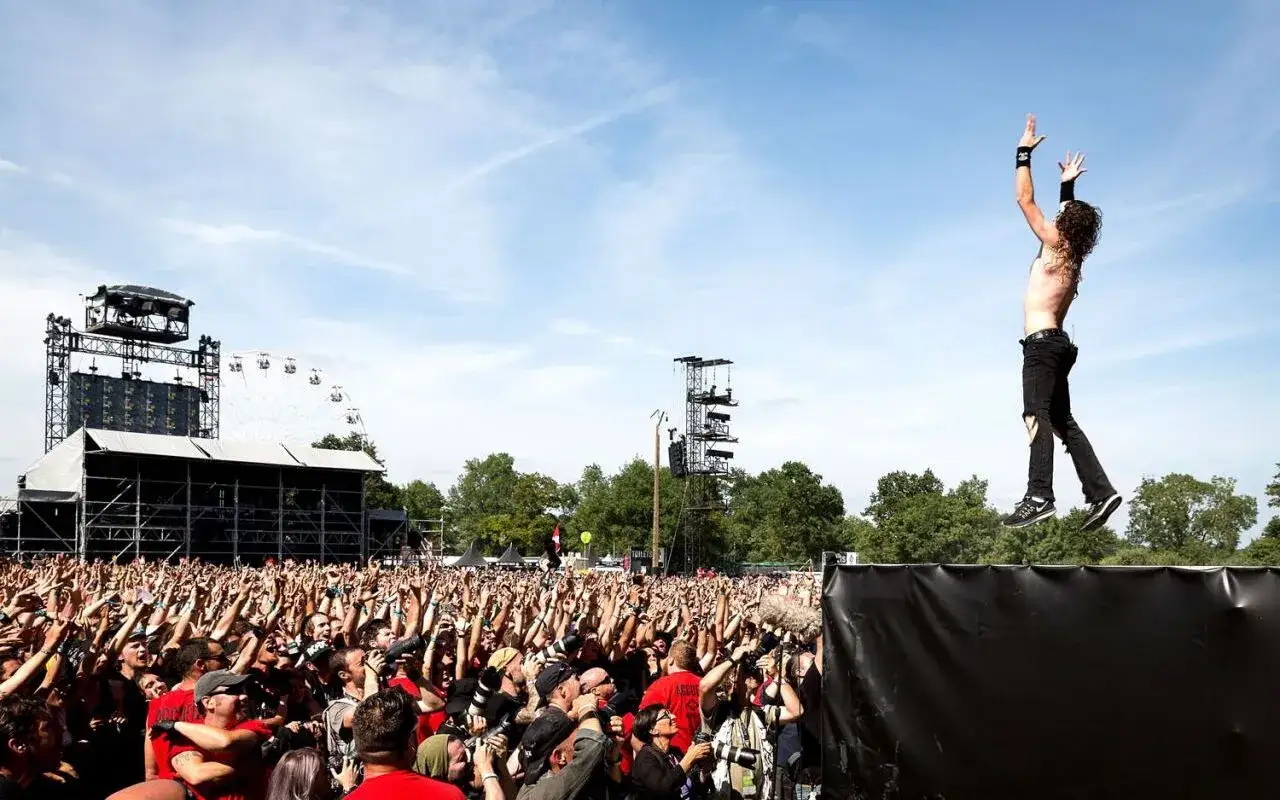 Un chanteur d'un groupe metal fran&ccedil;ais connu saute au-dessus d'une foule en d&eacute;lire, sous un ciel bleu.