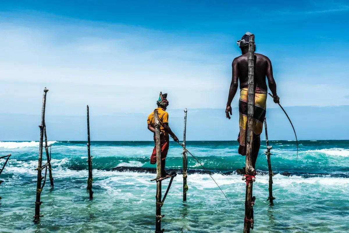 Zwei Stelzenfischer in Sri Lanka balancieren auf Pfählen im Meer, um Fische zu fangen.