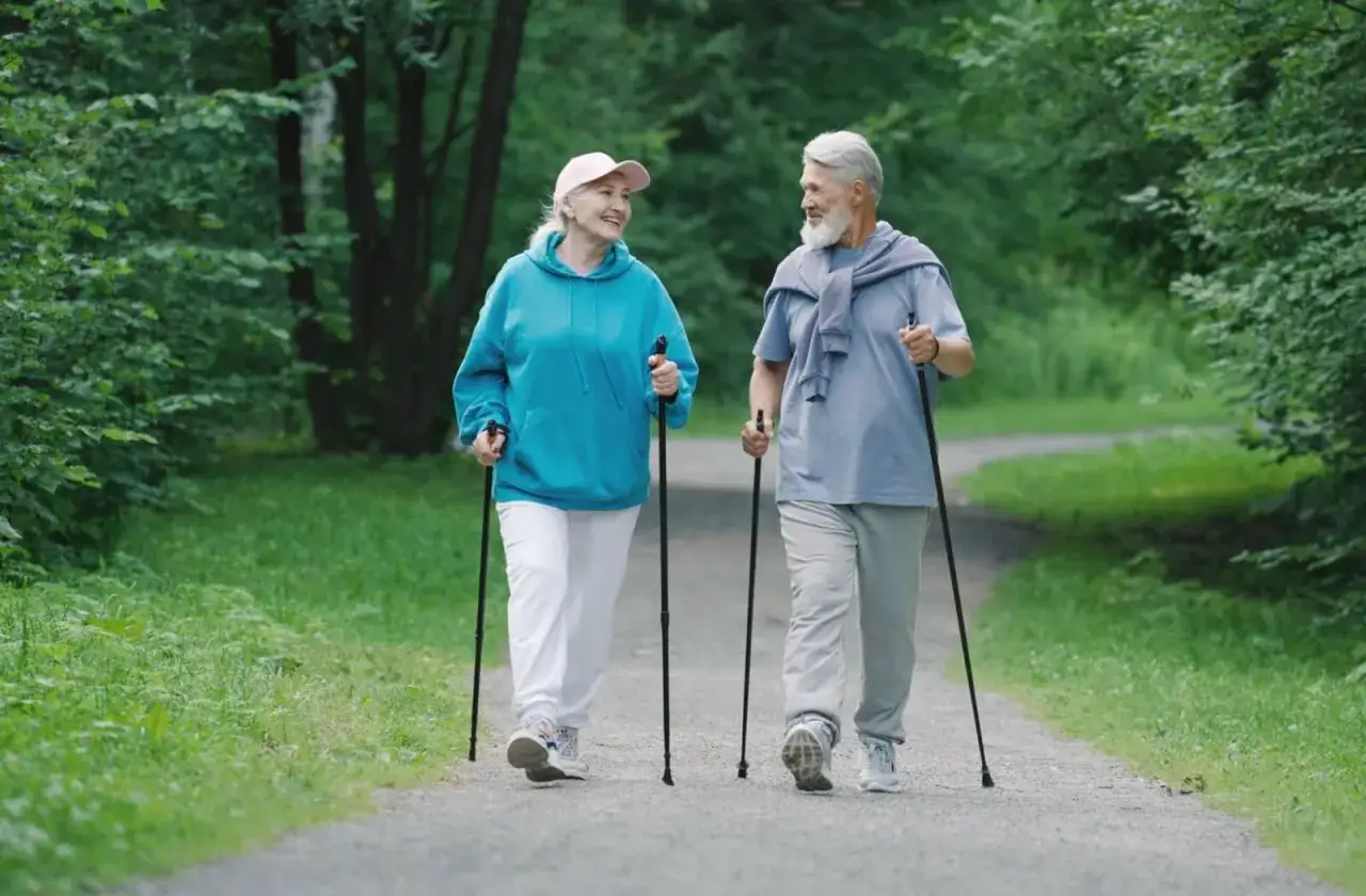 Uśmiechnięta para senior&oacute;w uprawia nordic walking w parku. To świetny spos&oacute;b na aktywność, choć wymaga pewnej wprawy.