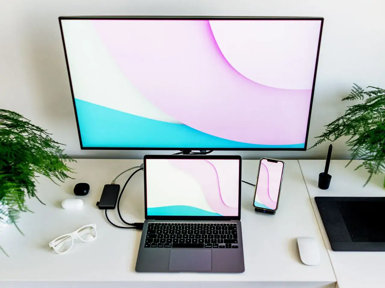 Ein Schreibtisch-Setup mit einem gro&szlig;en Monitor, einem Laptop als Monitor genutzt, Smartphone, Kopfh&ouml;rern und Pflanzen.