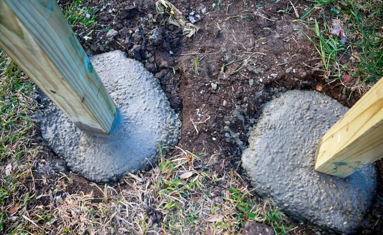 Zwei Holzpfosten werden gerade in frisch gegossenen Beton gesetzt, um sie sicher zu verankern. Das Einbetonieren von Zaunpfosten sorgt für Stabilität.