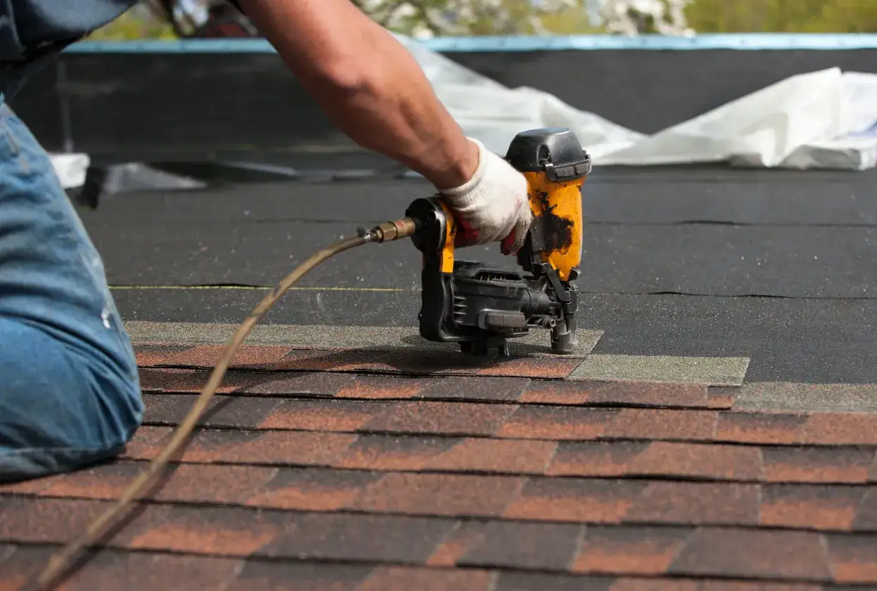 A roofer demonstrates how to shingle a roof, using a nail gun to secure asphalt shingles.