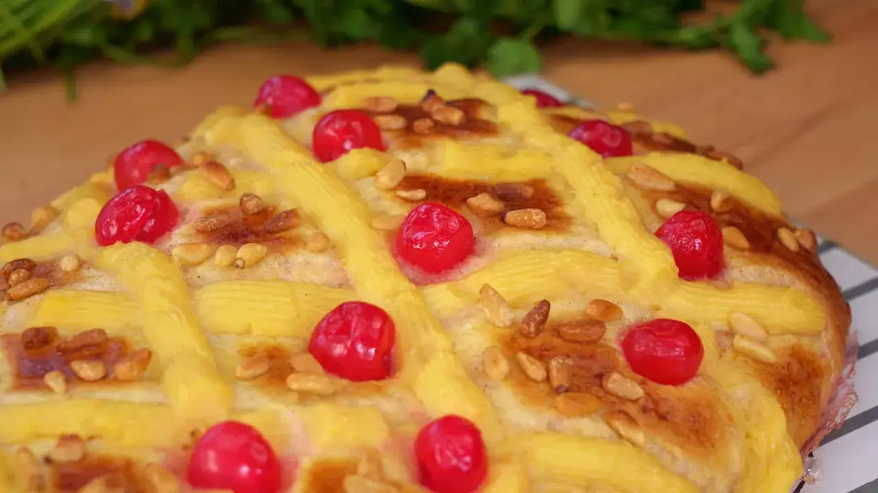 Deliciosa coca de Sant Joan decorada con crema, piñones y cerezas rojas.