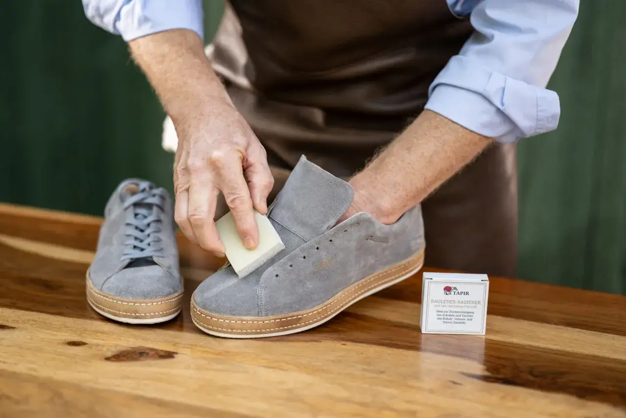 Mann reinigt graue Nubukleder-Sneaker mit einem speziellen Radierer. Was ist das? Raulederpflege!