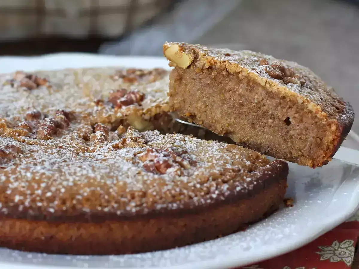 Un g&acirc;teau aux noix moelleux, saupoudr&eacute; de sucre glace, est servi. Une part est soulev&eacute;e, r&eacute;v&eacute;lant sa texture.