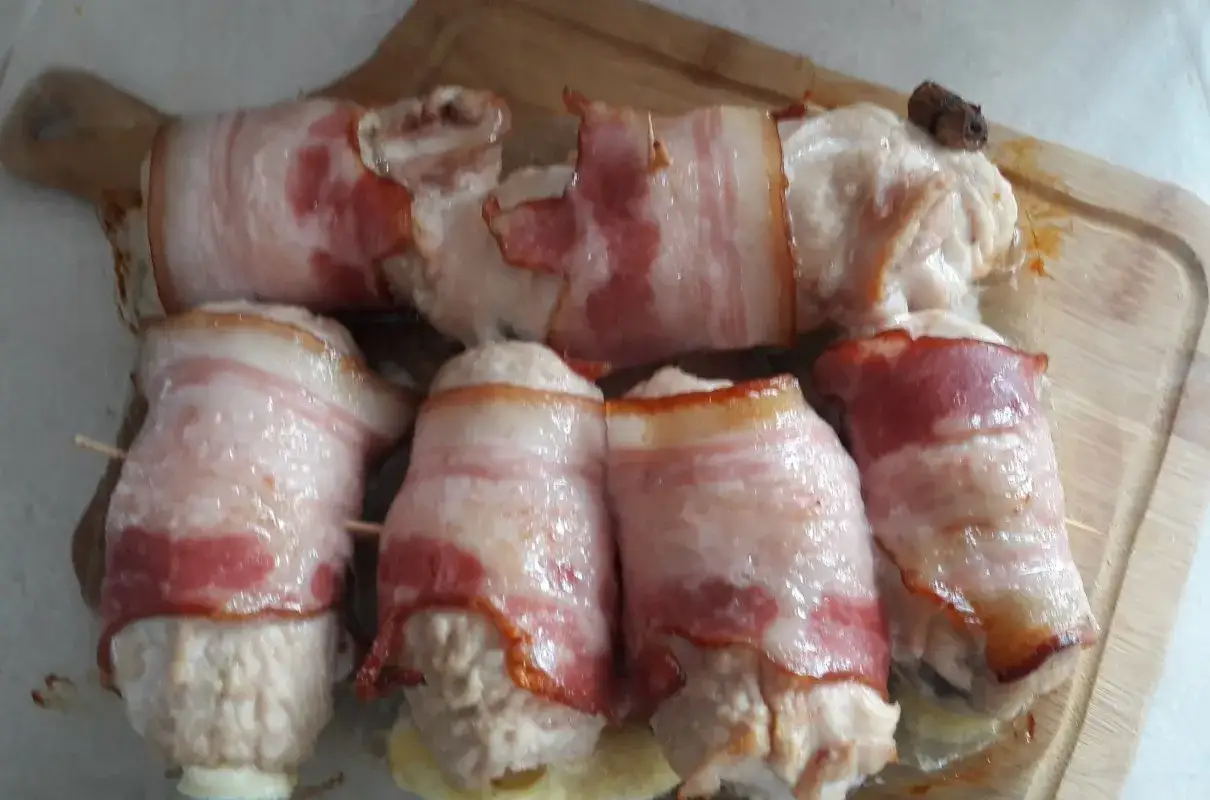 Roladki z indyka z boczkiem, gotowe do pieczenia, ułożone na desce.